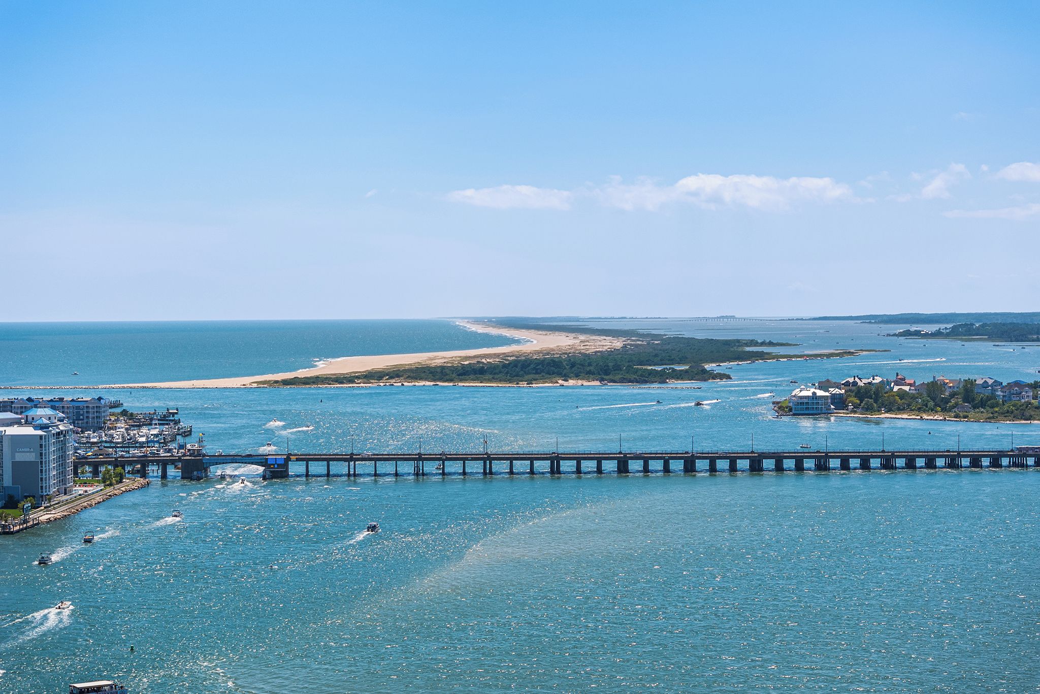 Un paysage urbain côtier avec une jetée imposante s’avançant dans la mer, une plage de sable et un ciel bleu dégagé.