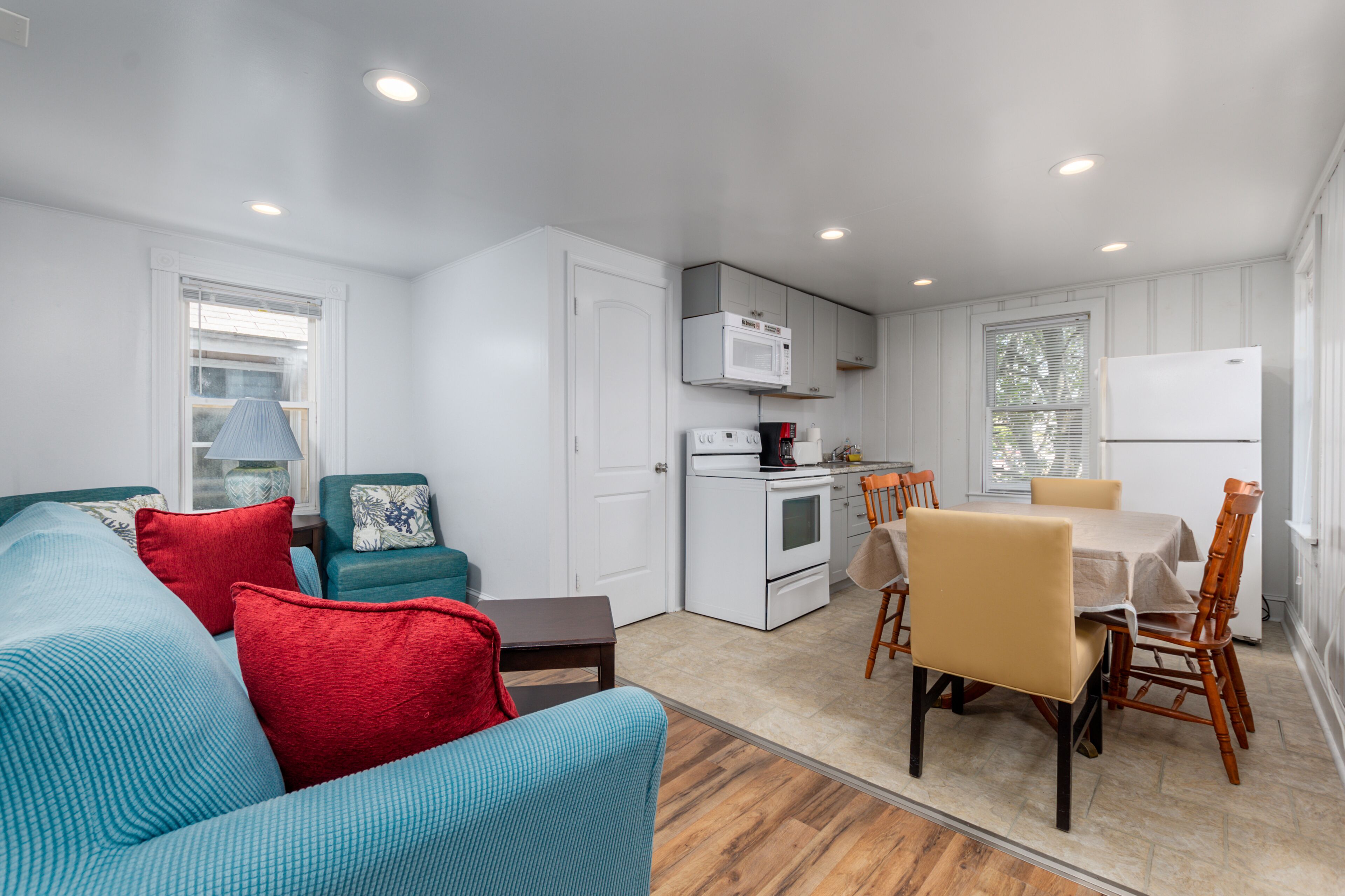 A compact living space with a kitchenette, a dining area with a table and chairs, and a sofa with cushions.