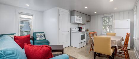 A compact living space with a kitchenette, a dining area with a table and chairs, and a sofa with cushions.