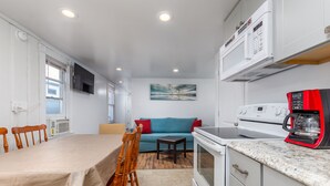 Una cocina compacta con una mesa de comedor, sillas, microondas, estufa y cafetera.