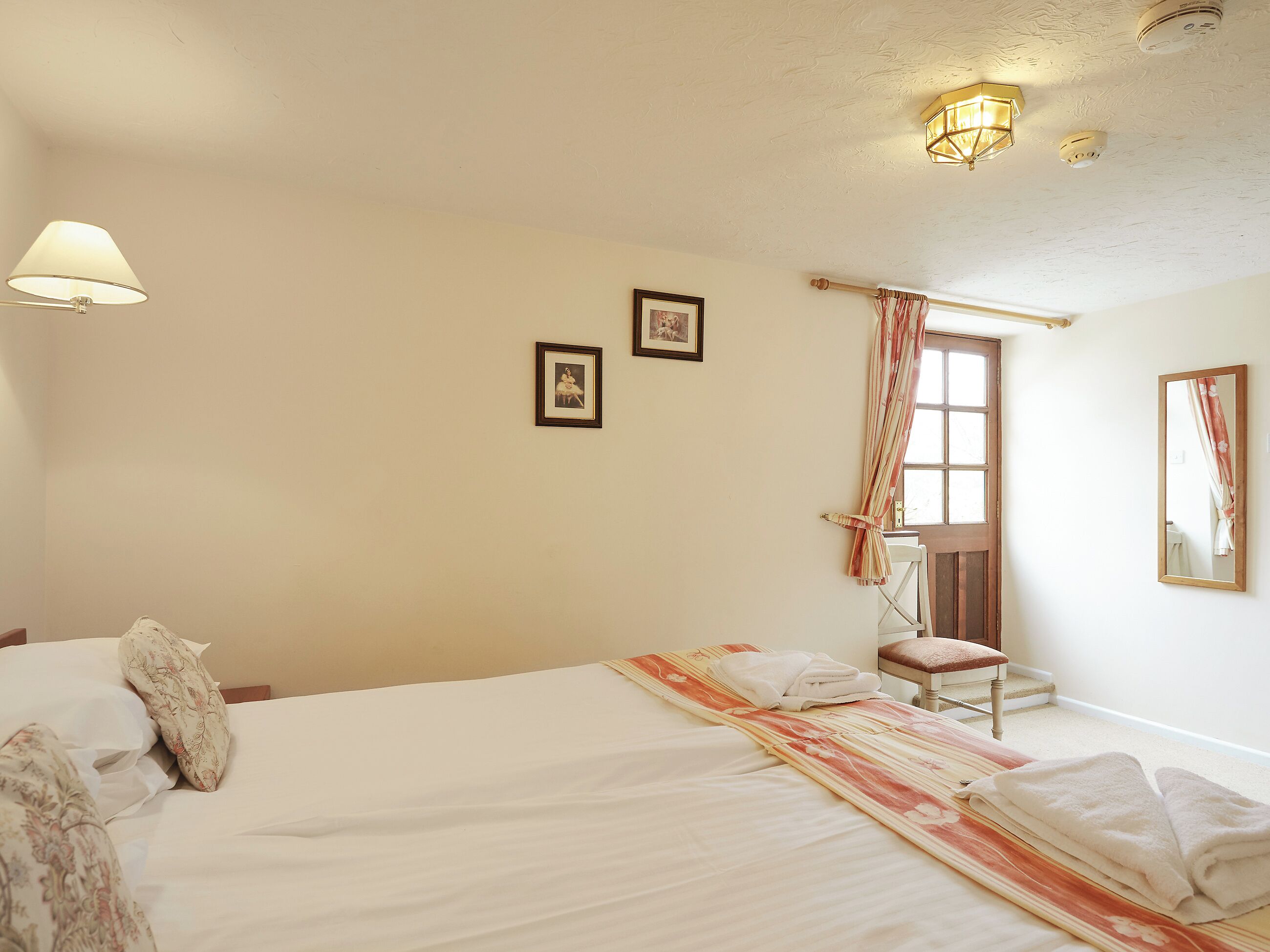 Een hotelkamer met een bed, een stoel, een raam met gordijnen en een spiegel aan de muur.