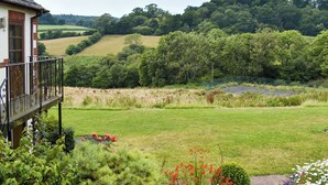 A house with a balcony overlooking a lush green landscape, including a tennis court and rolling hills. - 3 bedroom accommodation in Sidbury, near Sidmouth (Sidbury, near Sidmouth)
