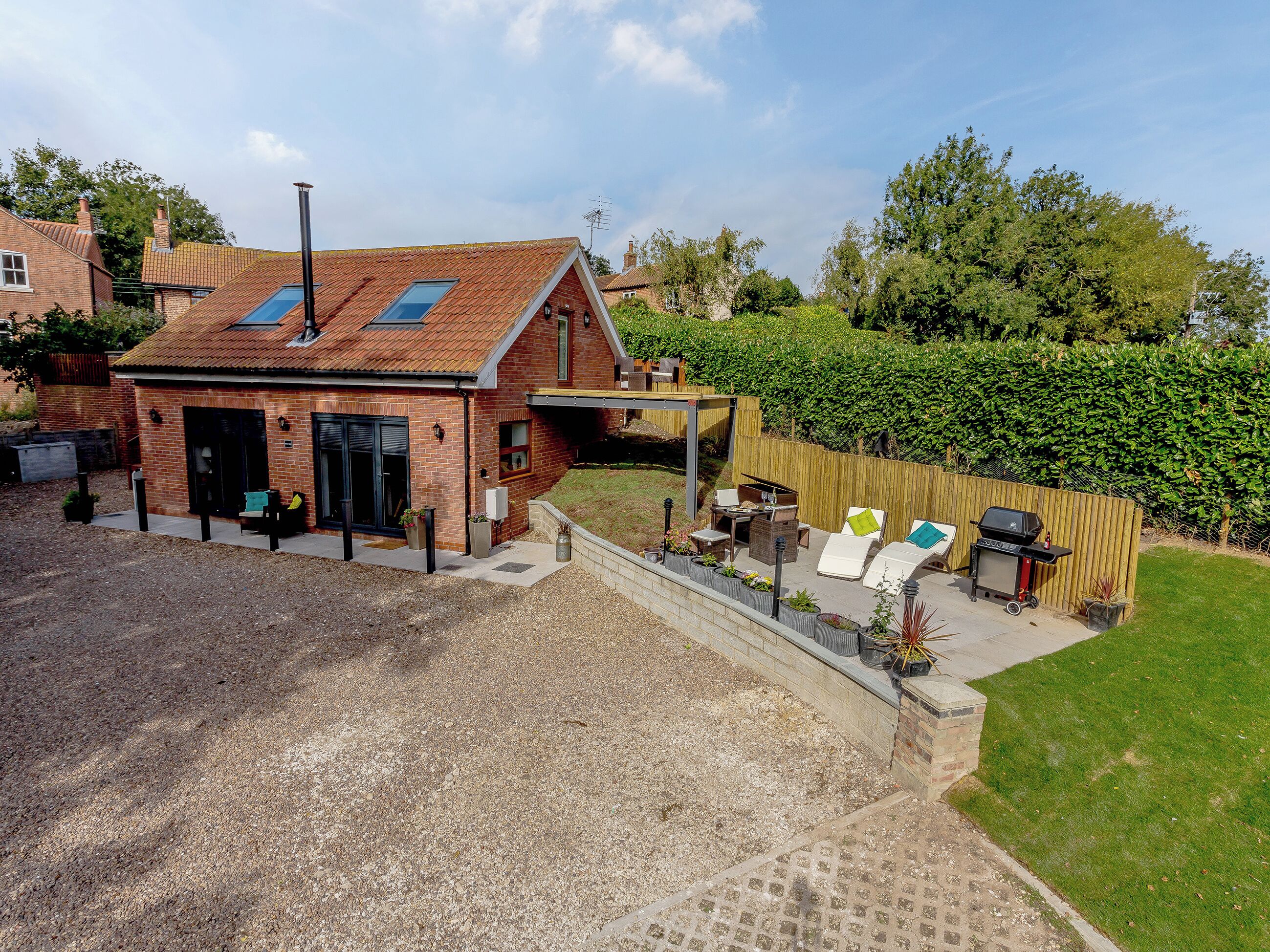 A brick house with a sloped roof, a covered patio area with outdoor furniture, and a well-maintained garden.