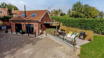 A brick house with a sloped roof, a covered patio area with outdoor furniture, and a well-maintained garden.