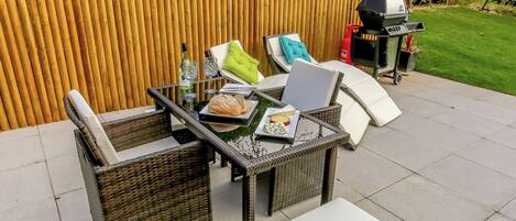 Un patio al aire libre con mobiliario de mimbre, una parrilla y una valla de madera.