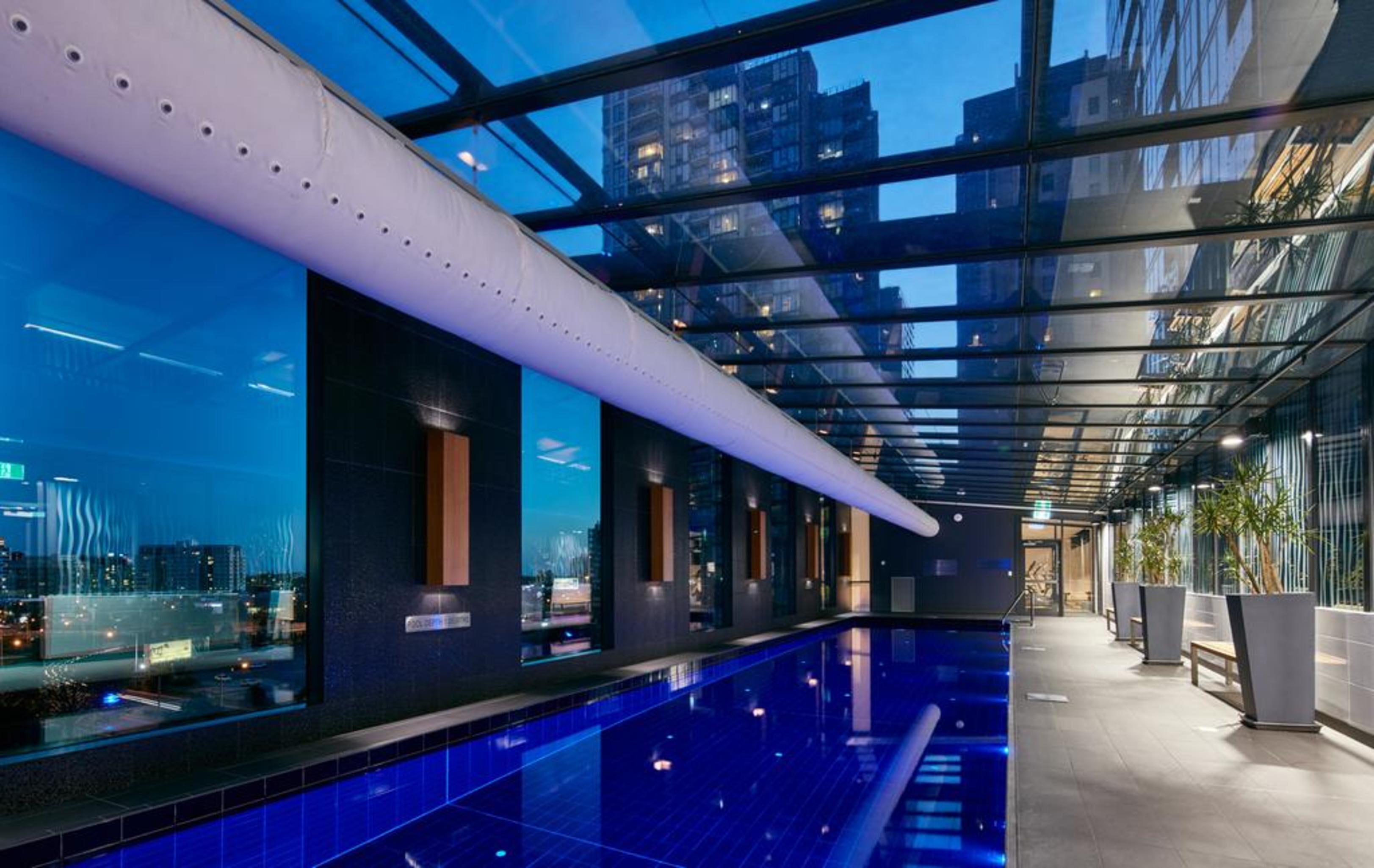 Un área de piscina interior moderna con techo de cristal, vistas a la ciudad y un diseño elegante.