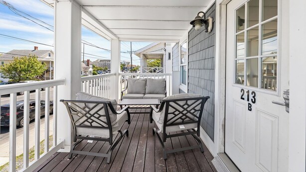 A covered porch with a wooden floor, two chairs, a table, and a sofa. - Spacious 3BR apartment 213B near Boardwalk and the Beach (Ocean City)