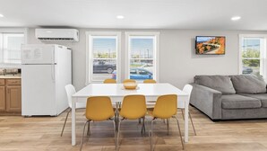 Een moderne keuken met een witte koelkast, een eettafel met vier gele stoelen en een grijze bank.