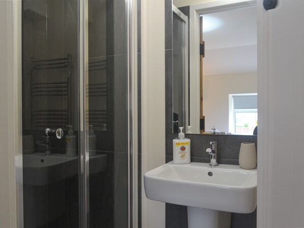 A bathroom with a glass shower enclosure, a white sink with a mirror above it, and a bottle of hand soap on the sink.