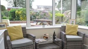 A corner seating area with wicker chairs and a glass table, a bottle of champagne, and a tray of pastries. - 2 bedroom accommodation in Bryncrug, near Tywyn (Bryncrug, near Tywyn)