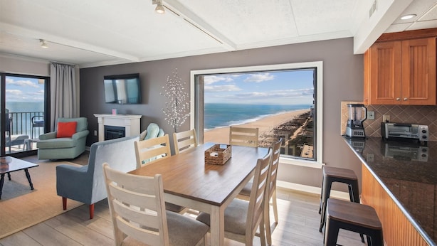 Una sala de estar moderna con una gran mesa de comedor, sillas de madera, un televisor y vista a la playa.