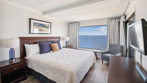 Habitación de hotel con una cama grande, un escritorio, una silla, un televisor y una ventana con vista al mar.