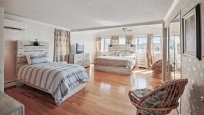 A spacious bedroom with a large bed, a wooden headboard, a TV, and a window with curtains.