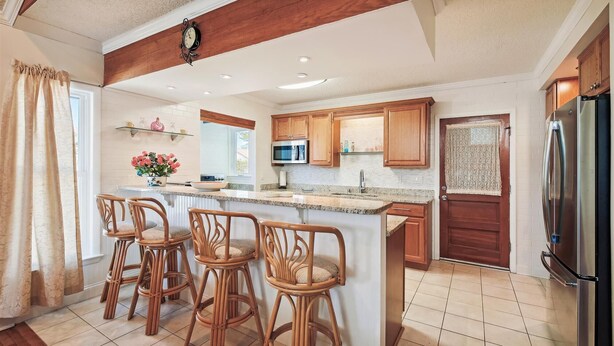 A kitchen with a central island, wooden bar stools, a microwave, and a refrigerator.