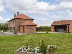 A brick house with a tiled roof, a covered outdoor seating area, and a well-maintained lawn with flower beds. - 2 bedroom accommodation in Ranby, near Retford (Ranby, near Retford)