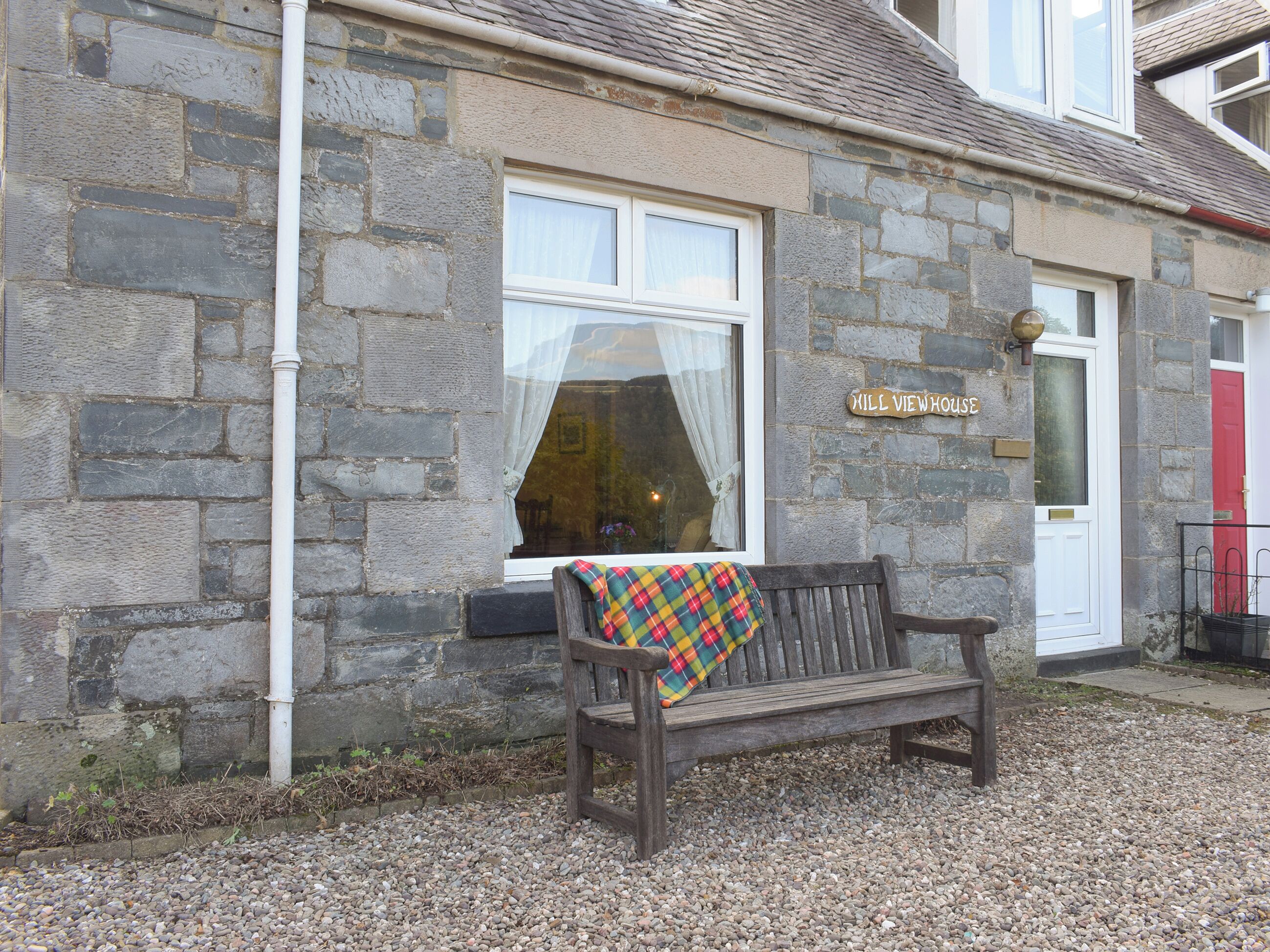 A stone building with a bench in front, a window with a curtain, and a sign reading "Hill Viewhouse".
