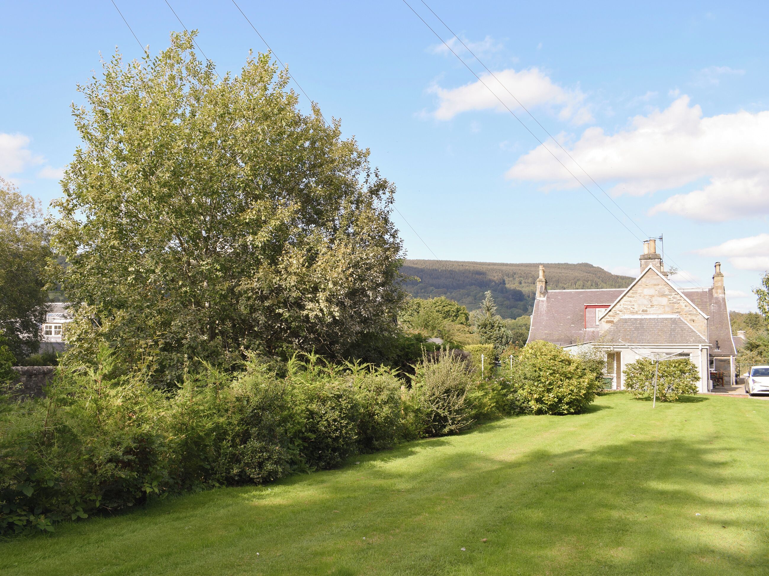 A rural house with a stone roof, surrounded by lush greenery and a clear sky.