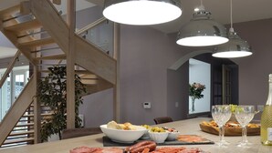 Un espace de restauration moderne avec un escalier en bois, une grande table dressée avec de la nourriture et des boissons, et des luminaires suspendus.