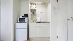 Une petite cuisine équipée comprenant un four à micro-ondes, un petit réfrigérateur, un évier et un plan de travail avec de la vaisselle et des produits de nettoyage.