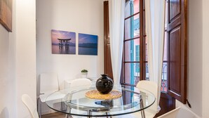 A modern dining area with a glass table and white chairs, a decorative vase, and two framed pictures on the wall.