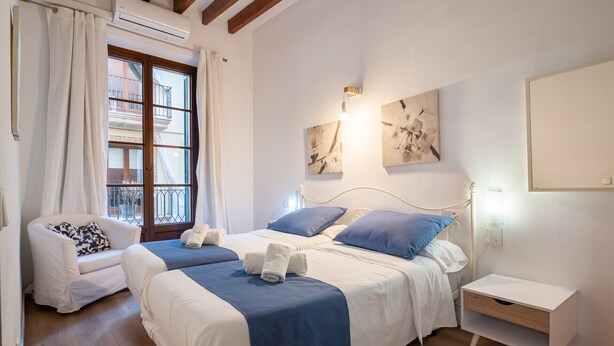 A bedroom with two beds, a chair, a bedside table, and a window with curtains.