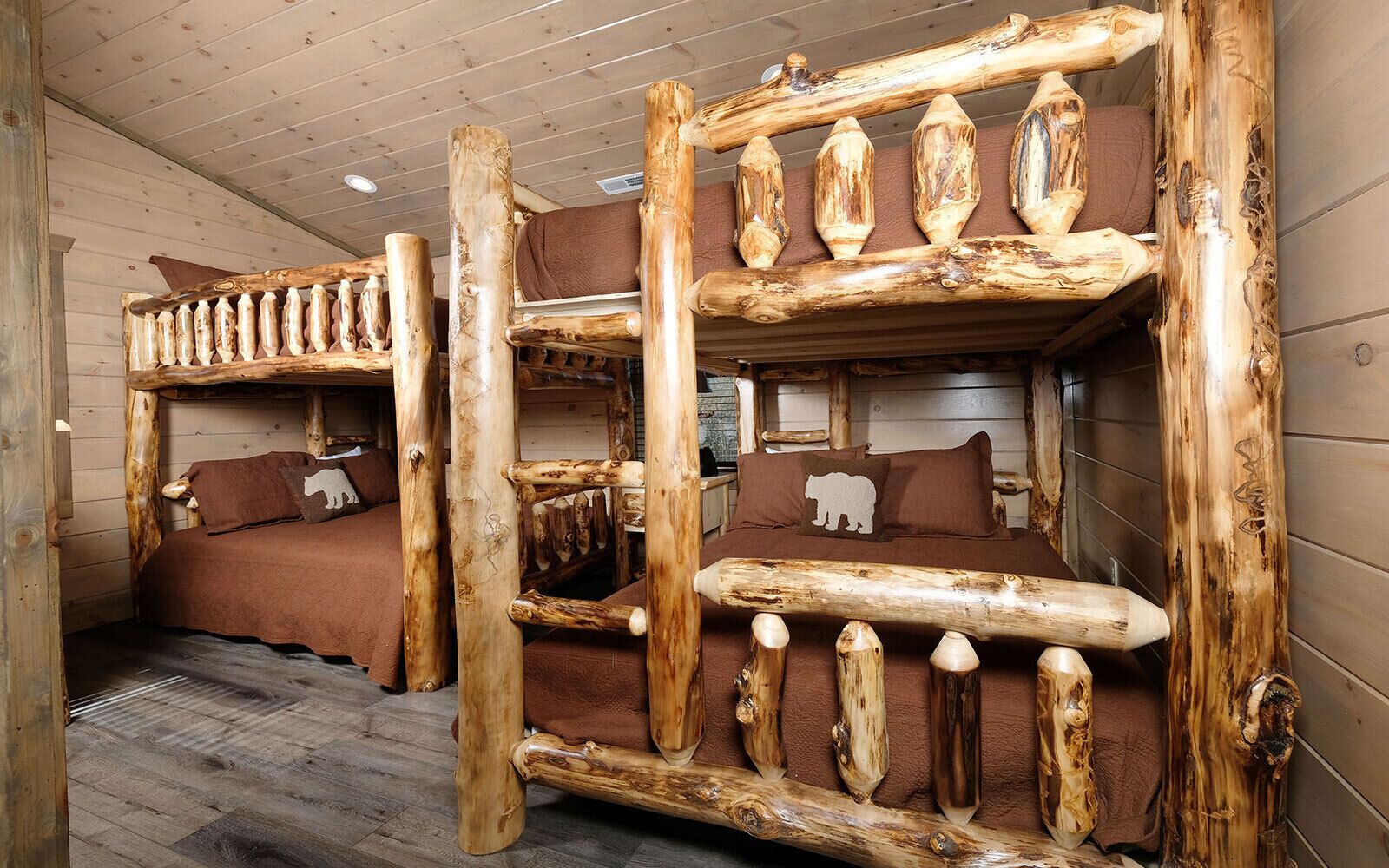 Eine Holzhütte mit zwei Etagenbetten aus Naturholz, jeweils mit einer braunen Matratze und einem Kopfkissen mit einer Bär-Silhouette.