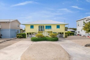 A two-story residential building with a flat roof, a front porch, and a small front yard with a hedge. - Waterfront Home w/ Private Heated Pool & 60` Dock (Marathon)