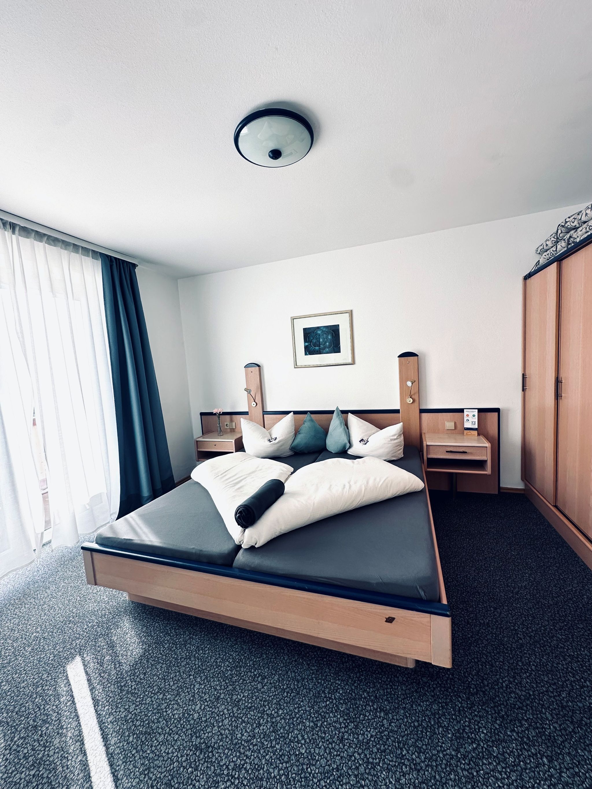 A hotel room with a bed, a bedside table, a nightstand, a wardrobe, and a ceiling light.