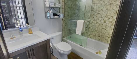 A modern bathroom with a glass-enclosed shower, a white toilet, and a vanity with a mirror.
