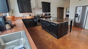 A modern kitchen with dark cabinetry, a central island, stainless steel appliances, and a potted plant.