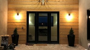 A building entrance with a wooden facade, a large antler skull decoration, and two potted plants on either side.