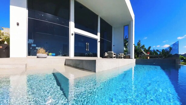 Une maison moderne dotée d’une piscine, de grandes fenêtres et de mobilier d’extérieur.