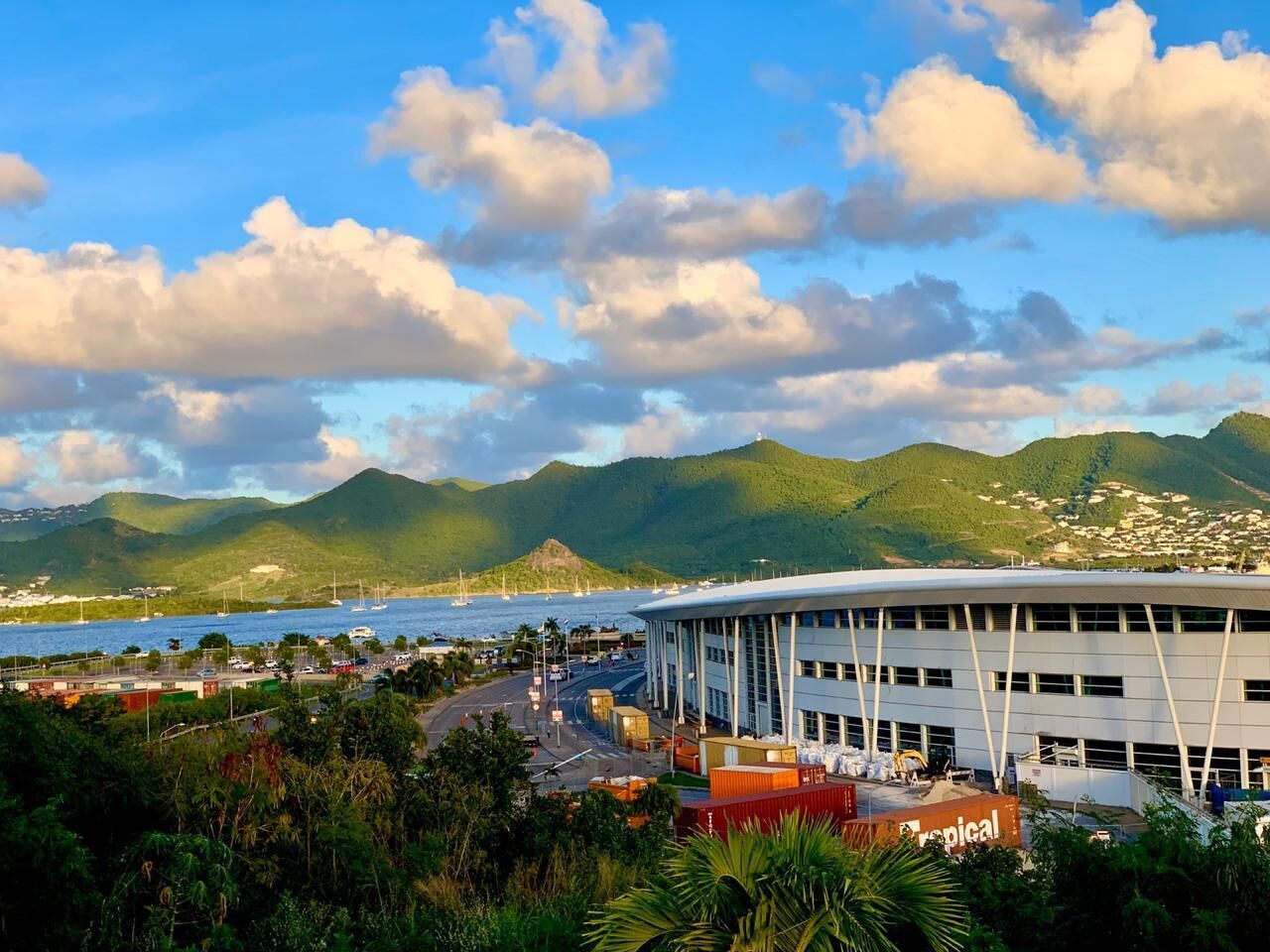 Un edificio moderno con techo curvo, rodeado de exuberante follaje y vistas al mar.