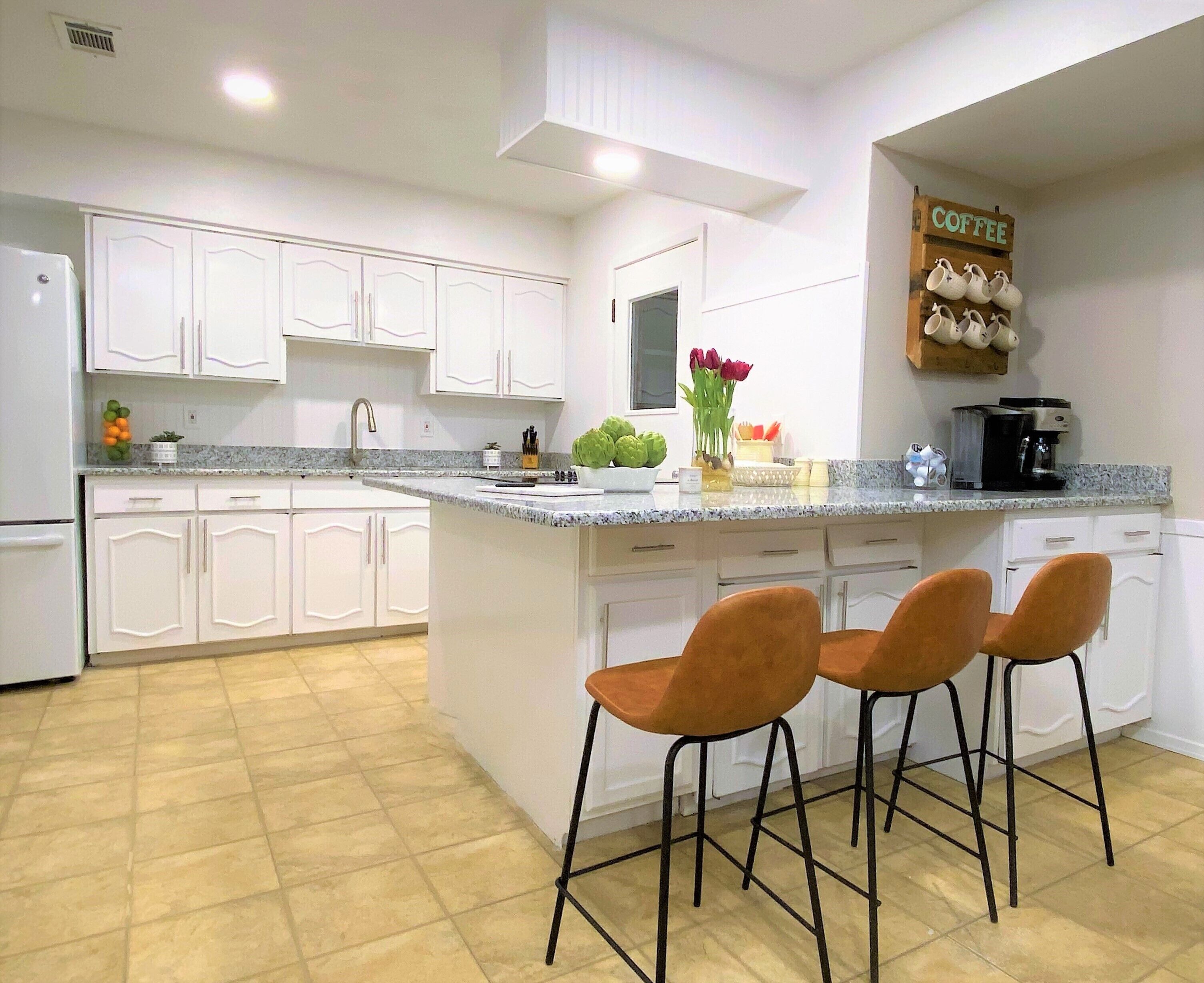 A modern kitchen with white cabinets, a granite countertop, and three orange bar stools.