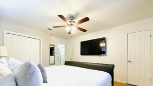 Ein Schlafzimmer mit Bett, Deckenventilator, Fernseher und weißen Türen.