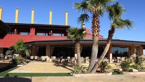 A hotel with outdoor seating, palm trees, and a red building with yellow chimneys. - Chateau Vinasoro (Alcazar de San Juan)