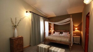 A four-poster canopy bed with a wooden headboard, bedside tables, and a nightstand. There are two upholstered ottomans in front of the bed. - Chateau Vinasoro (Alcazar de San Juan)