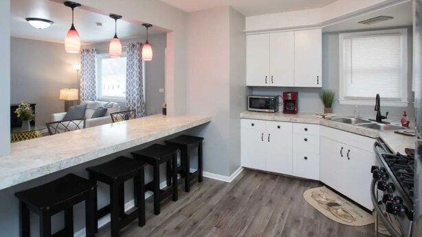 A modern kitchen with white cabinets, a marble countertop, black bar stools, a microwave, and a stove. - ❤️ Unbeatable group travel retreat ❤️ (Omaha)