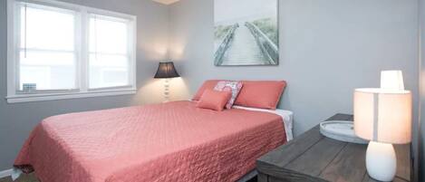 A bedroom with a bed, a nightstand, a lamp, a window, and a wall art piece.