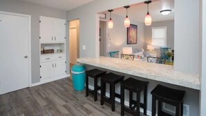A kitchen with a marble countertop, three black stools, white cabinets, and pendant lighting. - ❤️ Unbeatable group travel retreat ❤️ (Omaha)