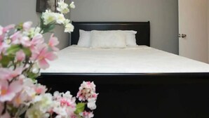 A neatly made bed with white bedding and a dark headboard in a room with a door and a wall-mounted light fixture. - ❤️ Unbeatable group travel retreat  ❤️ (Omaha)