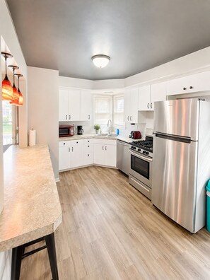 A modern kitchen with white cabinets, stainless steel appliances, and a wooden floor. - ❤️ Unbeatable group travel retreat ❤️ (Omaha)