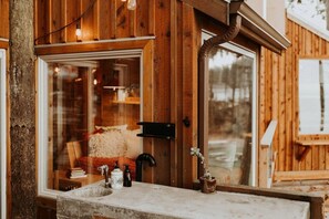 A wooden cabin with a stone sink, a mirror, and a window reflecting a cozy interior. - Perch small · Treehouse-Eagles Perch over the water (Port Angeles)