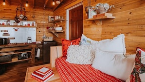 A cozy cabin interior with a wooden interior, a kitchenette, a sofa with red and white bedding, and a bookshelf. - Perch small · Treehouse-Eagles Perch over the water (Port Angeles)