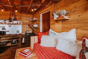 A cozy cabin interior with a wooden interior, a kitchenette, a sofa with red and white bedding, and a bookshelf.