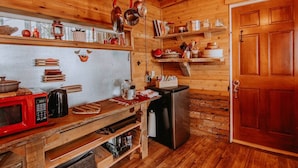 A wooden cabin kitchen with a red microwave, a coffee maker, and various utensils on shelves. - Perch small · Treehouse-Eagles Perch over the water (Port Angeles)