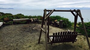 A wooden swing set and bench on a sandy beach with a view of the sea and distant land. - Perch small · Treehouse-Eagles Perch over the water (Port Angeles)