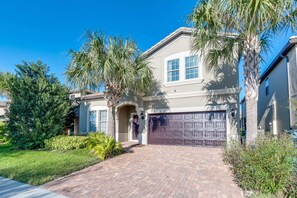 A two-story house with a brick driveway, a garage, and palm trees. - Sleek Home With Big Pool Area and Game Room, CDC Cleaning Standards #8ws105 (Kissimmee)