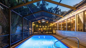 A covered swimming pool with glass walls, a poolside area with tables and chairs, and a view of trees outside. - 6BR! Sleeps 15+ Htd Pool, putting green, Theater, game rm, 5 mi to beaches, AMI (Bradenton)
