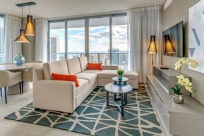A modern living room with a sectional sofa, a small round table, and a large window offering a city view. - NEW 2019 Condo, 1Bedroom+2 Bathrooms, Amazing Views@HydeResort (Hollywood)